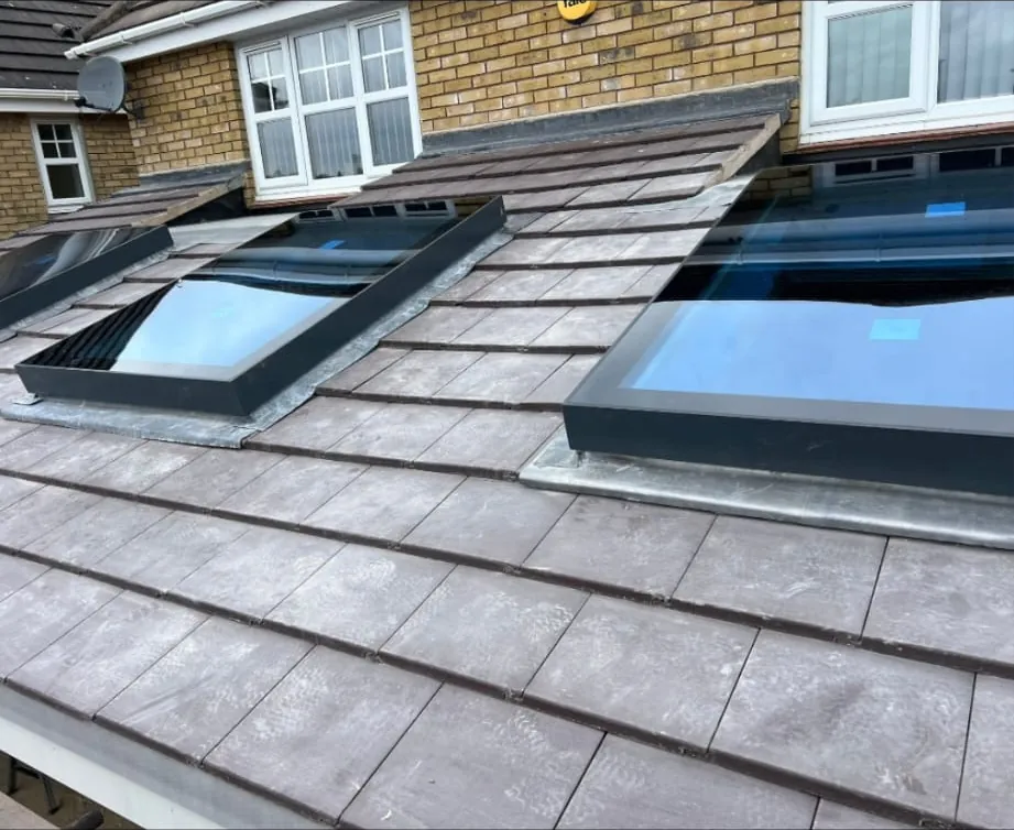 Two black flat glass rooflights set into a brown tiled roof