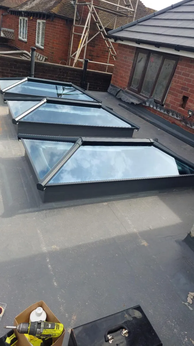Three aluminium roof lanterns in a row on a grey flat roof during installation